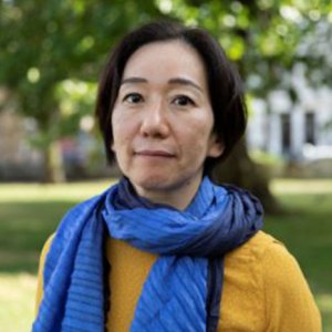Head shot of middle aged Japanese woman with ear length black hair and in a yellow jumper.